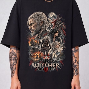 Peut inclure: Un t-shirt noir à manches courtes avec une impression graphique détaillée de The Witcher Wild Hunt. Le motif comprend plusieurs personnages, un paysage avec un phare, un médaillon de loup et le texte The Witcher Wild Hunt en argent et rouge.