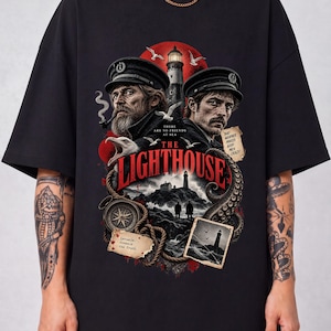 Puede incluir: Una camiseta negra con un estampado gráfico inspirado en The Lighthouse. El diseño incluye dos hombres con gorras de capitán, un faro, gaviotas, una brújula y una cuerda. El texto dice: There are no friends at sea, Bad weather makes good men crazy y Inviate reveals the truth.
