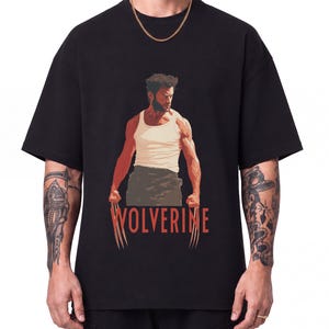 Könnte beinhalten: Ein schwarzes kurzärmeliges T-Shirt mit einem Grafikdruck eines muskulösen Charakters in einem weißen Unterhemd und dunkler Hose, mit ausgefahrenen Metallkrallen. Der Text WOLVERINE ist in roter Schrift unter dem Motiv gedruckt.