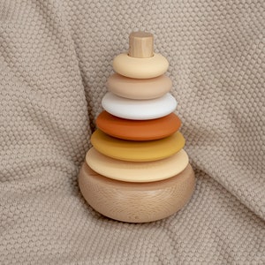 Può includere: Un giocattolo di impilamento in legno con sei anelli in varie tonalità di giallo, arancione e marrone. Gli anelli sono impilati su una base in legno.