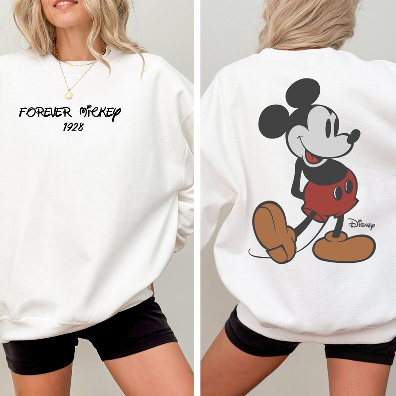 Puede incluir: Sudadera blanca con "FOREVER MICKEY 1928" en escritura negra en la parte delantera. La parte trasera muestra un gran gr&aacute;fico de Mickey Mouse en rojo, negro y marr&oacute;n, con el logotipo de Disney. Una prenda casual y c&oacute;moda.