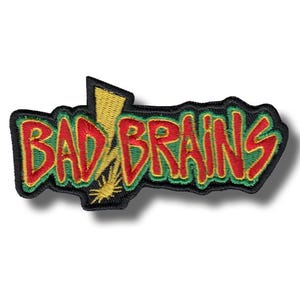 May include: An embroidered fabric patch featuring the text BAD BRAINS in red letters with a green outline. A yellow lightning bolt graphic is integrated into the design behind the letters. The entire patch is bordered by a thick black stitched edge.