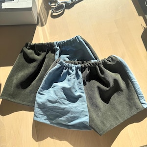 Op de afbeelding: Twee shorts met een color-block ontwerp met afwisselende panelen van olijfgroene corduroy en lichtblauwe stof. Elk paar heeft een elastische tailleband met geplooid materiaal, wat zorgt voor een zachte, gerimpelde textuur aan de bovenkant.