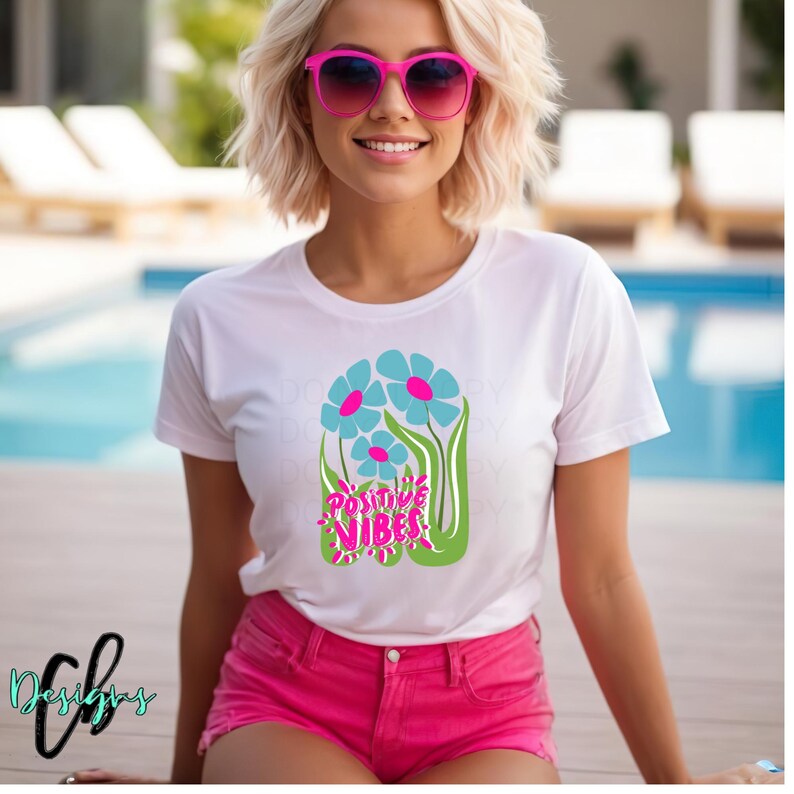 May include: White t-shirt with a floral design featuring blue and pink flowers and the words "Positive Vibes" in pink. The person is wearing pink sunglasses and pink shorts.
