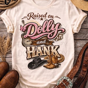 May include: Cream-colored t-shirt with the text "Raised on Dolly and Hank." The design includes a guitar, butterfly, musical notes, cowboy boots, a black hat, and a rope. A straw hat and a leather belt are also visible.
