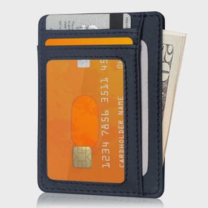May include: A navy blue leather cardholder wallet with multiple slots. One slot displays a credit card with the numbers 1234 7856 3511 45. Another slot holds a folded twenty-dollar bill. The wallet is designed for carrying cards and cash.