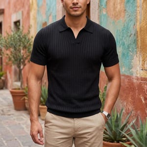 Puede incluir: Polo negro de manga corta con textura acanalada y cuello en V. La camisa se combina con pantalones color caqui. Se ve un reloj de pulsera plateado en la muñeca izquierda. El fondo presenta una pared colorida y texturizada y plantas en macetas.