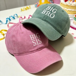 Puede incluir: Dos gorras de béisbol, una rosa y otra verde, apiladas. La gorra rosa tiene bordado en blanco "BIG SIS", mientras que la gorra verde tiene bordado en blanco "BIG BRO". Ambas gorras tienen viseras curvas y correas ajustables.