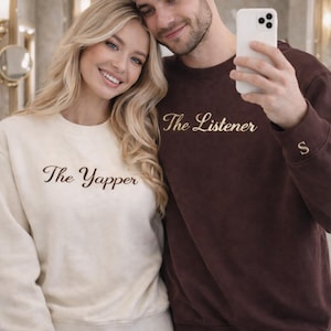 May include: A couple wearing matching sweatshirts. One is cream-colored with "The Yapper" embroidered in brown, the other is maroon with "The Listener" embroidered in gold. Both have a single initial on the cuff.