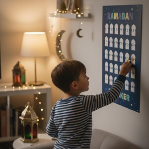 May include: A navy blue Ramadan calendar with white numbers and a star sticker. The calendar is hanging on a white wall. A young child is placing a star sticker on the calendar. The word "Ramadan" is at the top of the calendar.