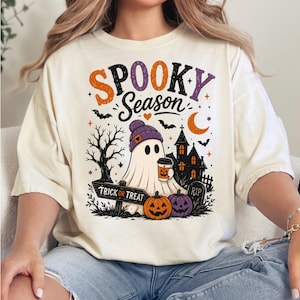 以下が含まれることがあります： SPOOKY SEASONという文字がプリントされたクリーム色のTシャツ。紫色のニット帽をかぶってコーヒーカップを持つお化け、お化け屋敷、コウモリ、三日月、カボチャ、TRICK OR TREATと書かれた看板が描かれたデザインです。