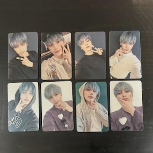 May include: Eight rectangular photo cards featuring a person with blue hair in various poses. The person is wearing different colored tops, including black, white, and purple. Some cards show the person making a peace sign or pointing.