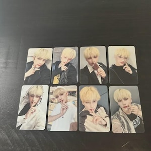 May include: Eight rectangular photo cards featuring a person with blonde hair in various poses and outfits. The cards are arranged in two rows of four on a dark surface. The person is holding a finger to their lips in some photos.