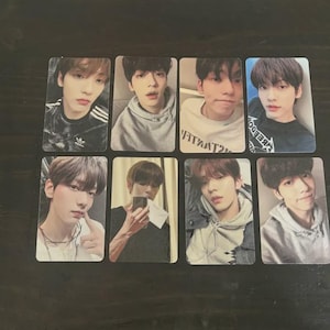 May include: Eight rectangular photo cards featuring images of a young person. The cards show the person in various poses, wearing different outfits, including a hoodie and a shirt with stripes. The photos are on a dark wooden surface.