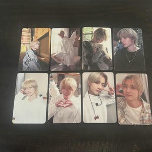 May include: A collection of eight photo cards featuring a person in various poses and settings. The cards showcase the person in different outfits, including casual wear and a white outfit with angel wings. The images have a soft, warm color palette.