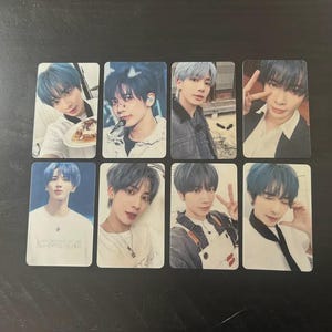 May include: A collection of eight rectangular photo cards featuring a young person with blue hair. The cards showcase different poses and expressions, with various outfits and backgrounds. The cards are arranged on a dark surface.