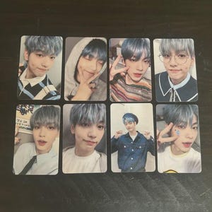 May include: Eight rectangular photo cards featuring a young person with blue hair. The cards show different poses and outfits, including a hoodie, glasses, and a denim jacket. The background is a plain, dark surface.