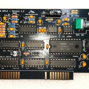 May include: Black circuit board labeled "ISA OPL2 - Version 1.2" with various electronic components, including chips, resistors, and capacitors. Features a Yamaha YM3812 chip and a green potentiometer.