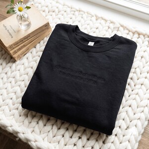 Könnte beinhalten: Ein schwarzer Rundhals-Pullover mit einer dunklen, ton-in-ton Stickerei auf der Brust, die den Text "please be patient with me I'm from the 1900s" zeigt. Das Kleidungsstück hat lange Ärmel, einen gerippten Ausschnitt und ein schlichtes Design.