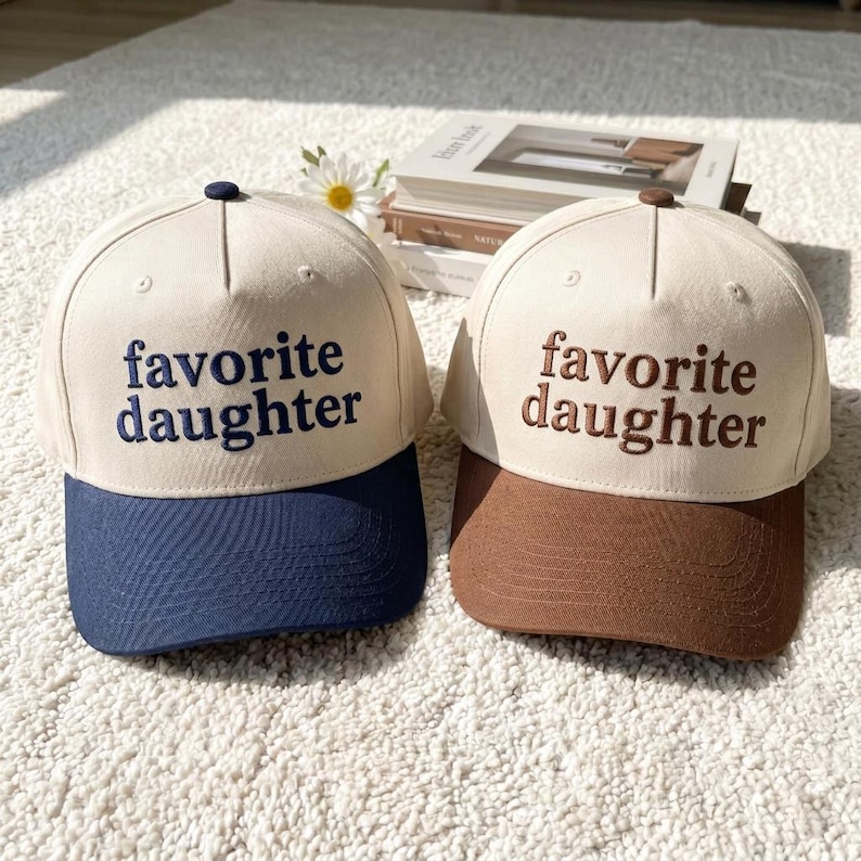 Puede incluir: Dos gorras de b&eacute;isbol con el texto "favorite daughter". Una gorra tiene una visera azul marino, la otra una visera marr&oacute;n. Ambas gorras tienen una corona color crema y el texto est&aacute; bordado.