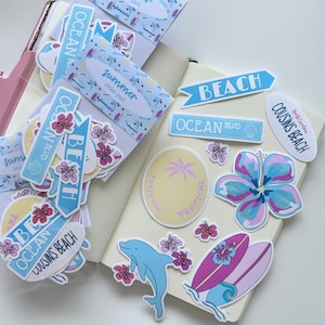 May include: A selection of summer-themed stickers with surfboard, dolphin, and floral designs. The stickers feature text such as "Beach," "Ocean Blvd," and "Cousins Beach." The colour palette includes blue, pink, and purple.