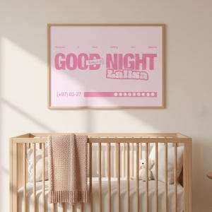 May include: A framed pink print with the words "GOOD NIGHT Lalisa" in a bold, playful font. The print also includes a phone number and a series of dots. The print is displayed above a wooden crib with a blanket and pillows.