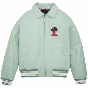 K&ouml;nnte beinhalten: Hellgr&uuml;ne Lederjacke mit Rei&szlig;verschluss, Kragen und gerippten B&uuml;ndchen und Saum. Die Jacke hat einen Brustaufn&auml;her mit einem Schilddesign und dem Text "AVIREX".