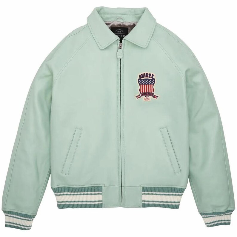 K&ouml;nnte beinhalten: Hellgr&uuml;ne Lederjacke mit Rei&szlig;verschluss, Kragen und gerippten B&uuml;ndchen und Saum. Die Jacke hat einen Brustaufn&auml;her mit einem Schilddesign und dem Text "AVIREX".