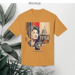 Puede incluir: Camiseta de color mostaza con un diseño gráfico. El diseño incluye un retrato de una mujer, el Capitolio de los Estados Unidos y la palabra "PIONEERED". El diseño incorpora rayas verticales en rojo, blanco y azul.