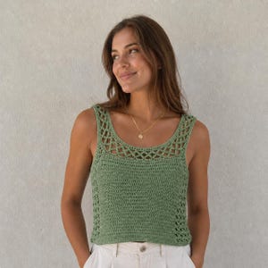 Peut inclure: Un débardeur en crochet vert sauge sans manches avec une large encolure dégagée, présentant un motif en treillis ajouré complexe sur le haut de la poitrine et les côtés, ainsi qu'un corps en maille crochetée dense et un collier chaîne doré.