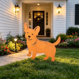 Puede incluir: Decoración de jardín de metal naranja con forma de perro, de pie sobre un césped verde. El perro tiene orejas grandes, una cara sonriente y un collar. La casa tiene revestimiento blanco, una puerta negra y una corona.
