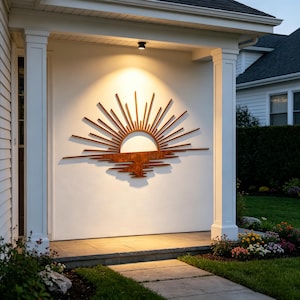 Puede incluir: Una gran pieza de arte mural de metal con forma de sol. El sol se representa con líneas radiantes y un semicírculo, con un reflejo debajo. La obra de arte está montada en una pared blanca, iluminada por un foco, y añade un toque decorativo.