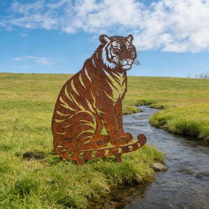 以下が含まれることがあります： 草地と小川のそばに、大きな錆びた金属製のトラの彫刻が座っています。 トラは、詳細な切り抜きの縞模様と顔の特徴を持つ座った姿勢です。 空は青く、雲が散らばっています。