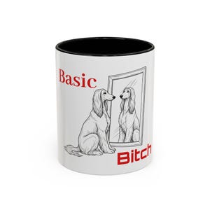 May include: White ceramic mug with a black interior, featuring a sketch of a dog looking in a mirror. The words "Basic" and "Bitch" are printed in red.