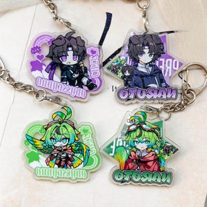 Op de afbeelding: Vier acryl sleutelhangers met personages in anime-stijl. Twee tonen een donkerharig personage met paarse ogen, gelabeld 'ODYSSEUS' en 'OTUSAN'. Twee tonen een groenharig personage met groenblauwe ogen, gelabeld 'ODYSSEUS' en 'OTUSAN', met kleurrijke vleugels.