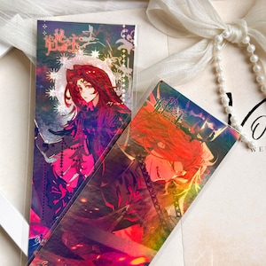 May include: Two rectangular bookmarks featuring vibrant anime-style illustrations of characters with long red hair. The designs incorporate holographic foil accents, intricate star patterns, and stylized Chinese text characters set against dark, dramatic backgrounds.