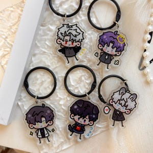 May include: Five acrylic keychains featuring chibi-style characters with black circular rings. The characters have distinct hair colors including white, purple, and dark brown, wearing suits or casual outfits with small graphic details like crowns or hearts.