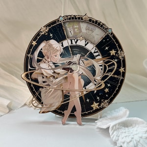 May include: A circular acrylic display featuring an anime-style elf character with long white hair, wearing a white outfit and reading a book. The background is a dark blue clock face with gold Roman numerals, stars, and orbital rings.