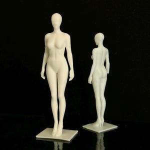 May include: Two white, 3D-printed female mannequin forms. One mannequin is viewed from the front, the other from the back. Both stand on square bases against a black background. The mannequins are smooth and detailed.