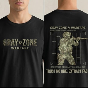 Op de afbeelding: Zwart t-shirt met de tekst "GRAY ZONE WARFARE" in camouflage-stijl letters op de voorkant. De achterkant heeft een soldatengrafiek en de tekst "GRAY ZONE // WARFARE", met coördinaten en de zin "TRUST NO ONE. EXTRACT FAST."