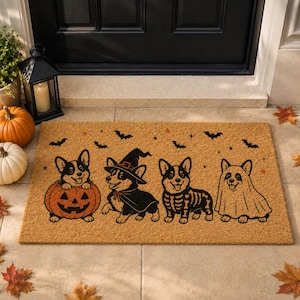 May include: A rectangular tan coir doormat featuring a black ink illustration of four Corgi dogs in Halloween costumes. The dogs are depicted as a pumpkin, a witch, a skeleton, and a ghost, surrounded by small black bats and orange stars.