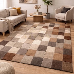 May include: A large, rectangular area rug with a checkered pattern in shades of brown, beige, and cream. The rug is placed on a hardwood floor in a living room setting, with a sofa, armchair, and coffee table visible in the background.