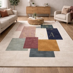 Op de afbeelding: Een groot, rechthoekig vloerkleed met een crèmekleurige achtergrond en geometrische vormen in verschillende kleuren. De vormen omvatten vierkanten en rechthoeken in tinten roze, groen, blauw en goud. Het vloerkleed ligt op een houten vloer.