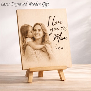 Peut inclure: Cadeau en bois gravé au laser. L'image montre une mère et son enfant sur une plaque de bois avec les mots "I love you Mom" et un symbole de cœur. La plaque est présentée sur un petit chevalet en bois.