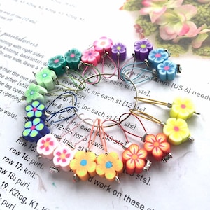 May include: A set of colourful flower-shaped stitch markers for knitting or crocheting. The markers are made of polymer clay and have a metal loop for attaching to yarn.