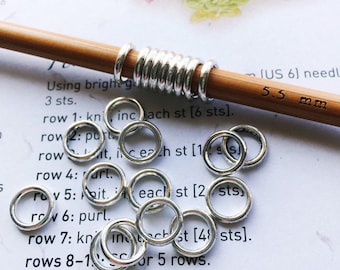 May include: Silver knitting stitch markers on a wooden knitting needle. The needle is labeled "US 6" and "5.5 mm".