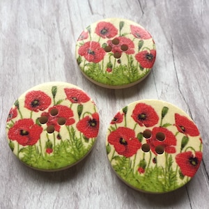 May include: Three round wooden buttons with a floral design. The buttons feature a white background with red poppies and green leaves. Each button has four holes.
