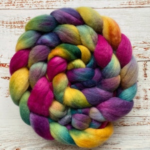 May include: A colorful braid of yarn in shades of purple, pink, yellow, green, and blue. The yarn is arranged in a spiral shape.