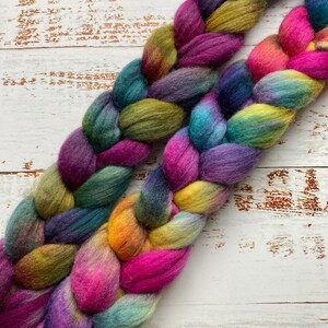 May include: Two strands of colorful hand-dyed yarn are braided together. The yarn is a mix of purple, pink, teal, green, and yellow.