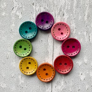 May include: A set of eight colourful wooden buttons with two holes each. The buttons are arranged in a circle on a white background. The buttons are in shades of pink, purple, green, yellow, and orange.